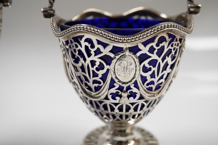 Two George III pierced silver pedestal sugar baskets, with blue glass liners, spiral handle, Burridge Davenport, London, 1777, the other William Plummer, London, 1775, tallest 10.1cm excluding the handle.